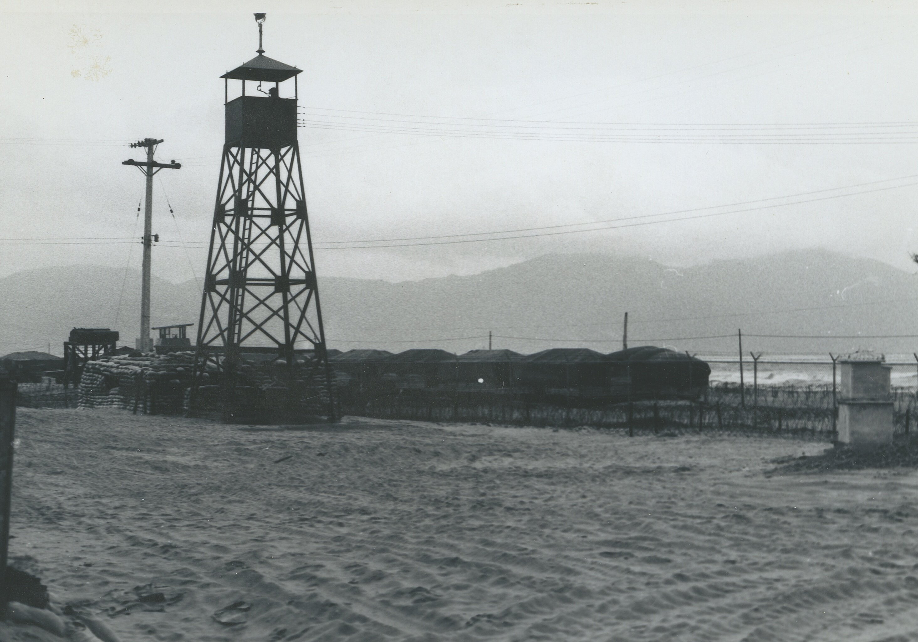 A guard tower and phone lines with a mountain in the background.