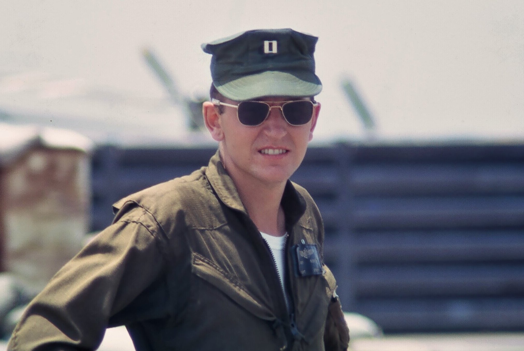 A young soldier wearing a cap, a flight jacket, and aviator sunglasses.