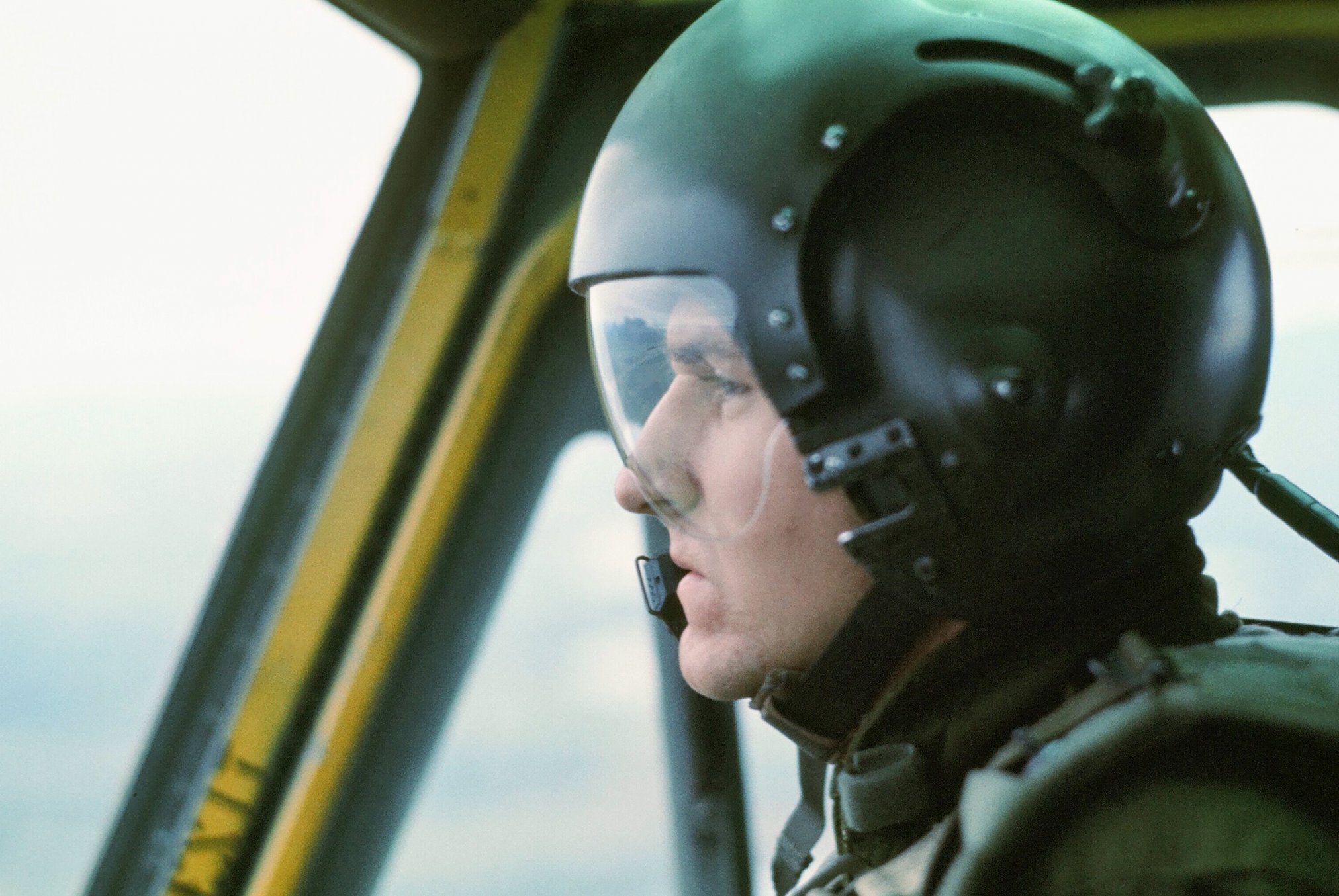 A profile of a young pilot in a plane, wearing a helmet and goggles.