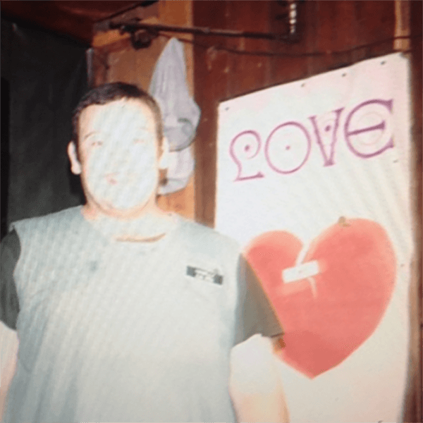 An overexposed photo of a large man in military scrubs standing in front of a poster that says "LOVE" and has a breaking heart on it.