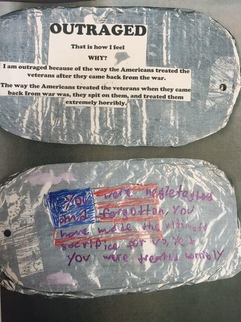 Close up of two "dog tag" middle school projects. "Outraged. That is how I feel. Why? Because of the way the Americans treated the veterans..." And "You were neglected and forgotten, you have made the ultimate sacrifice for us, yet you were treated horribly."