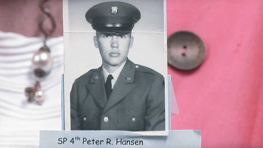 Official military portrait of a young, stoic man, being held up by a woman. Photo has a crease through it and text reads "SP 4th Peter R. Hansen."