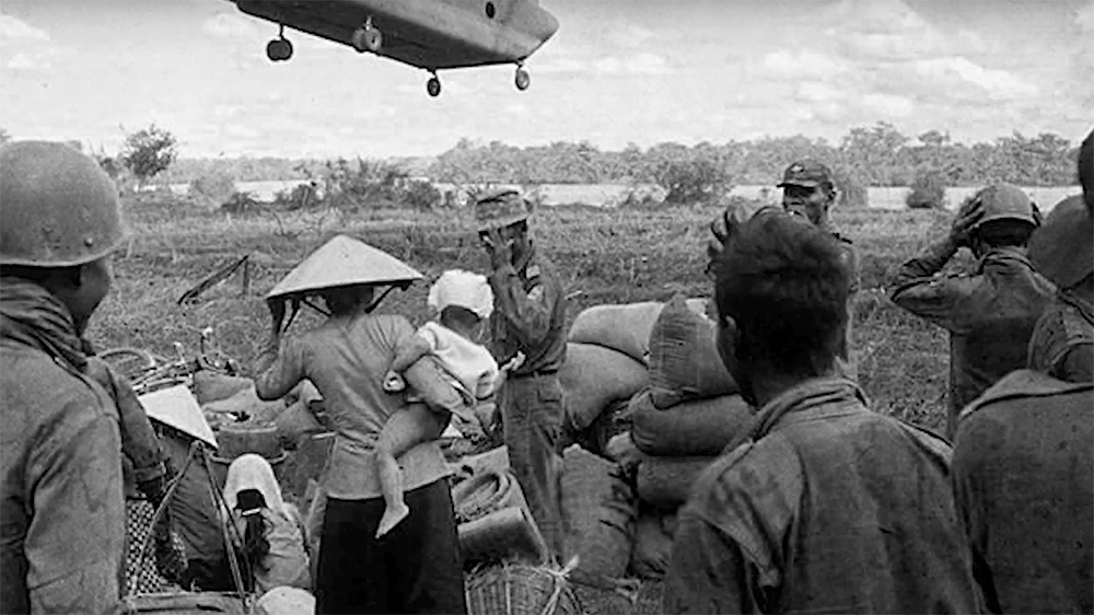 A Chinook helicopter overhead with Vietnamese civilians and soldiers on the ground below.