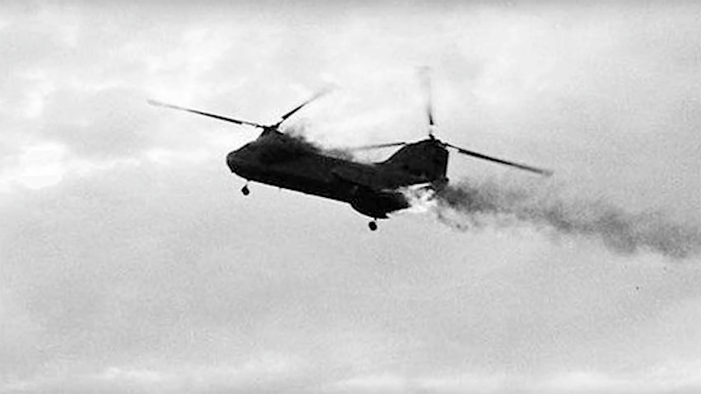 A Chinook helicopter in the sky, on fire and smoking.