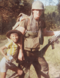 A U.S. soldier with a young Asian child leaning and hanging on him.