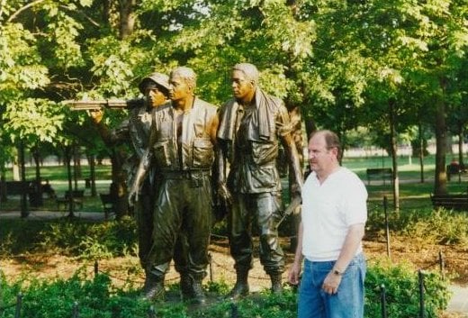 A man standing off to the side of of a memorial statue of three soldiers.