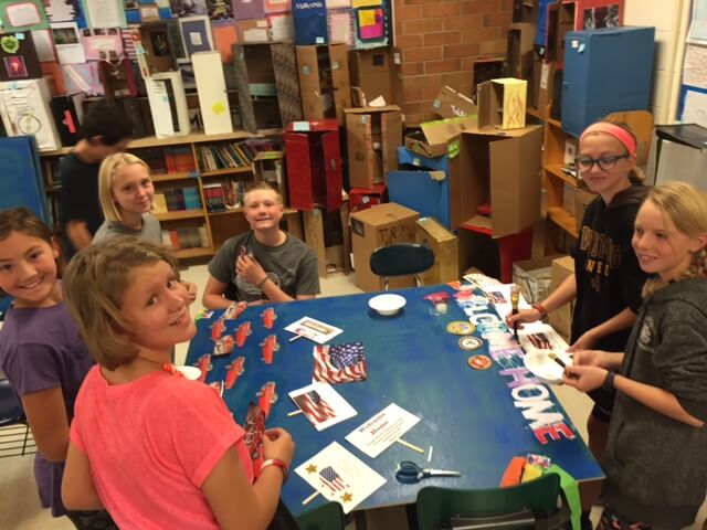 Contemporary image of middle school girls and a boy around a classroom table, decorating a patriotic-looking school project.