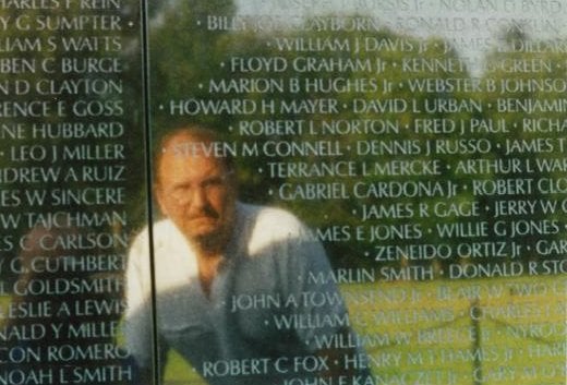 Reflection of a man in the Vietnam Wall. The name "Robert Norton" is near his head.