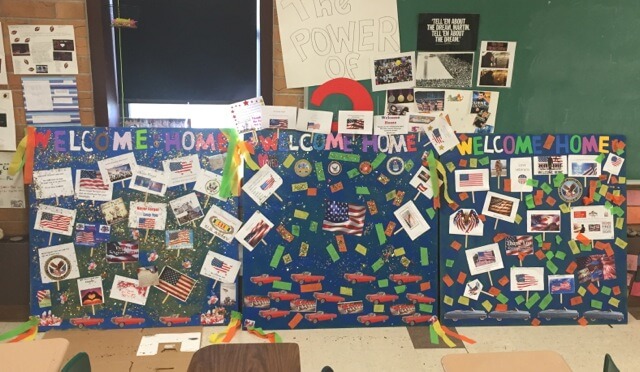 Contemporary image of three patriotic-looking boards that say "Welcome Home" and are decorated with flags, glitter, and imagery.
