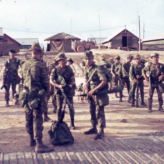 A group of U.S. and Asian soldiers in full gear, standing and waiting around.