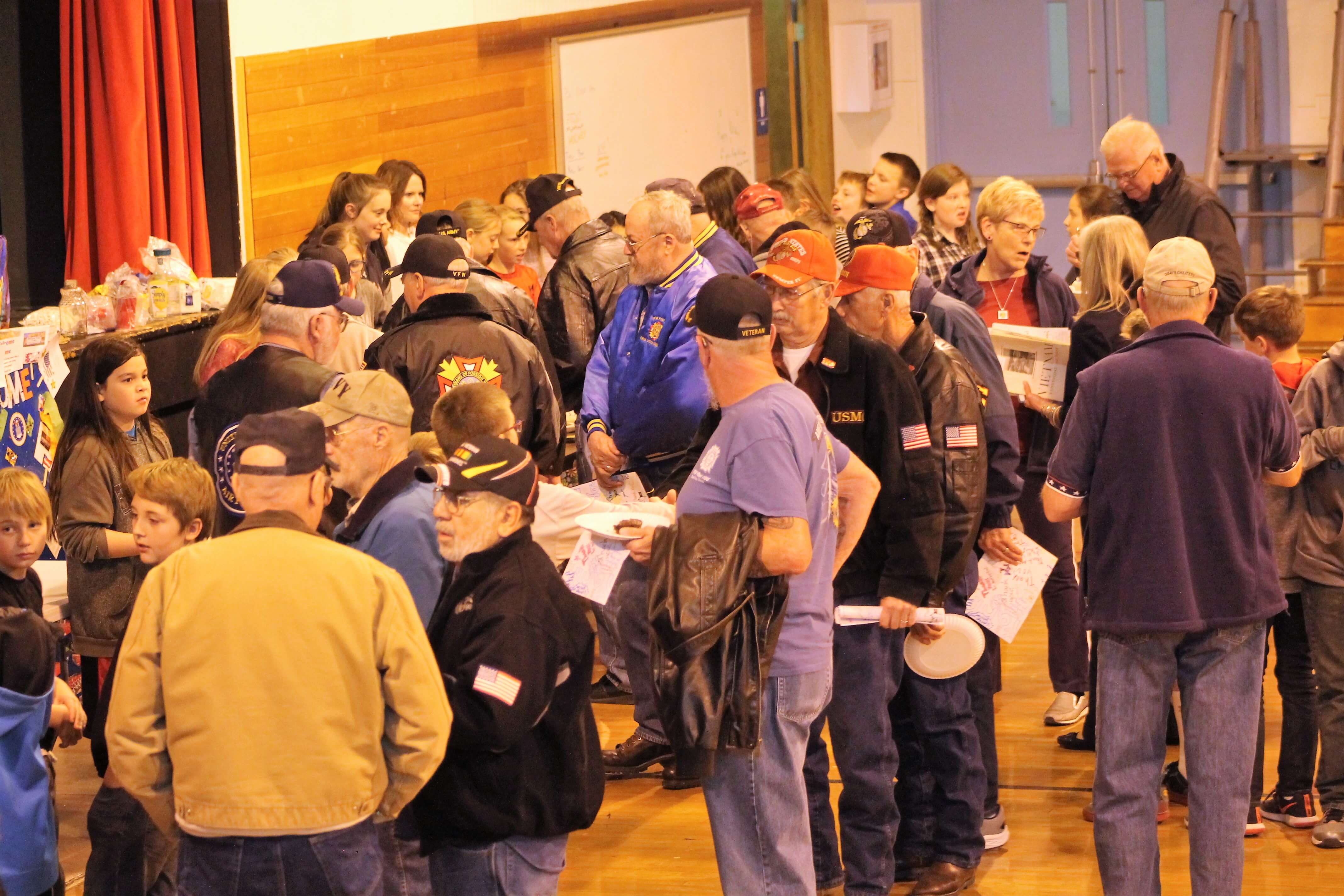 Contemporary image of veterans gathered in a gymnasium, eating from plates of food.