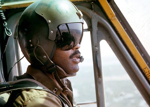 A young black pilot with his helmet and shades on, flying his aircraft.