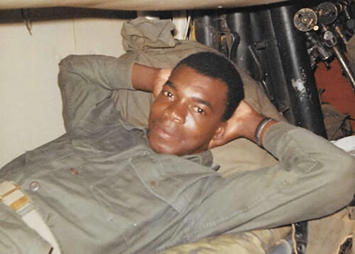 A young black soldier, laying with his hands behind his head.