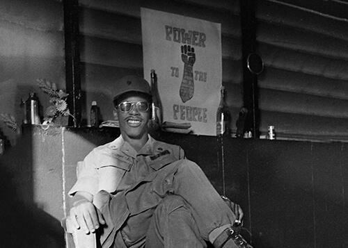 Black GI sitting in front of a Black Power poster.