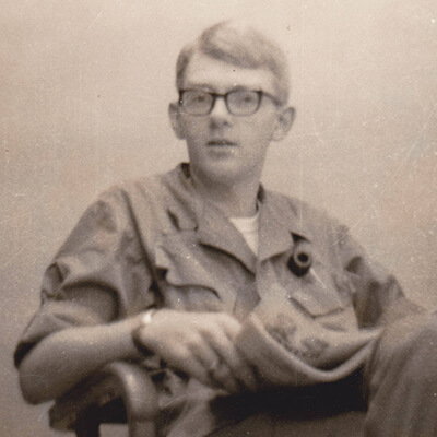 Portrait of a young soldier wearing glasses and looking up from his newspaper.