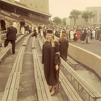 A young woman in a graduation cap and gown, with a white arm band tied around her left arm.