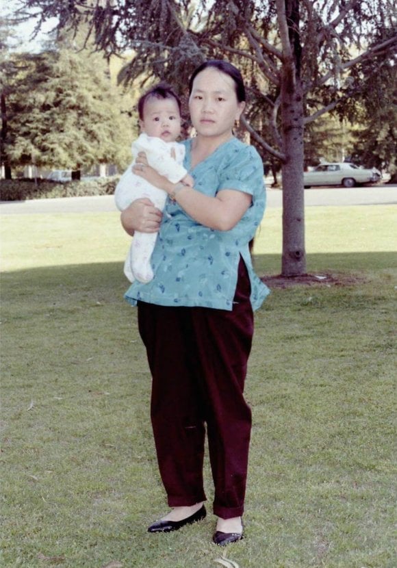 A Hmong woman standing outside holding a baby.
