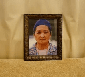 A framed portrait of a stern-looking, older Hmong woman.