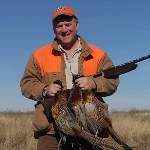 Contemporary photo of a man in hunting gear, holding a rifle and some pheasants.