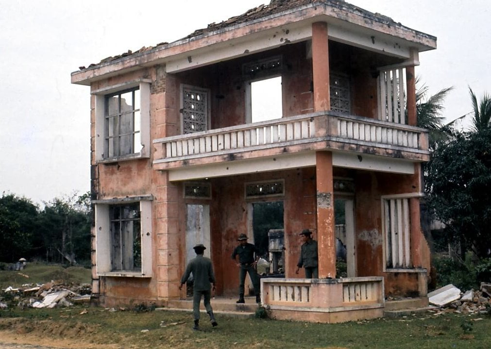 A small, two story pink building with three Asian man looking around the premises.