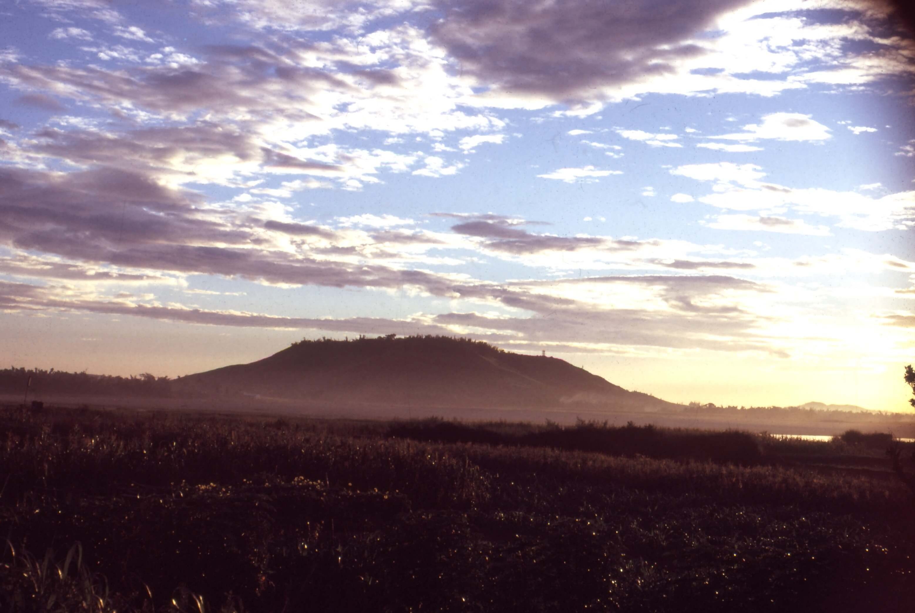 A field in the foreground, a foggy mountain in the background, and a sunrise.