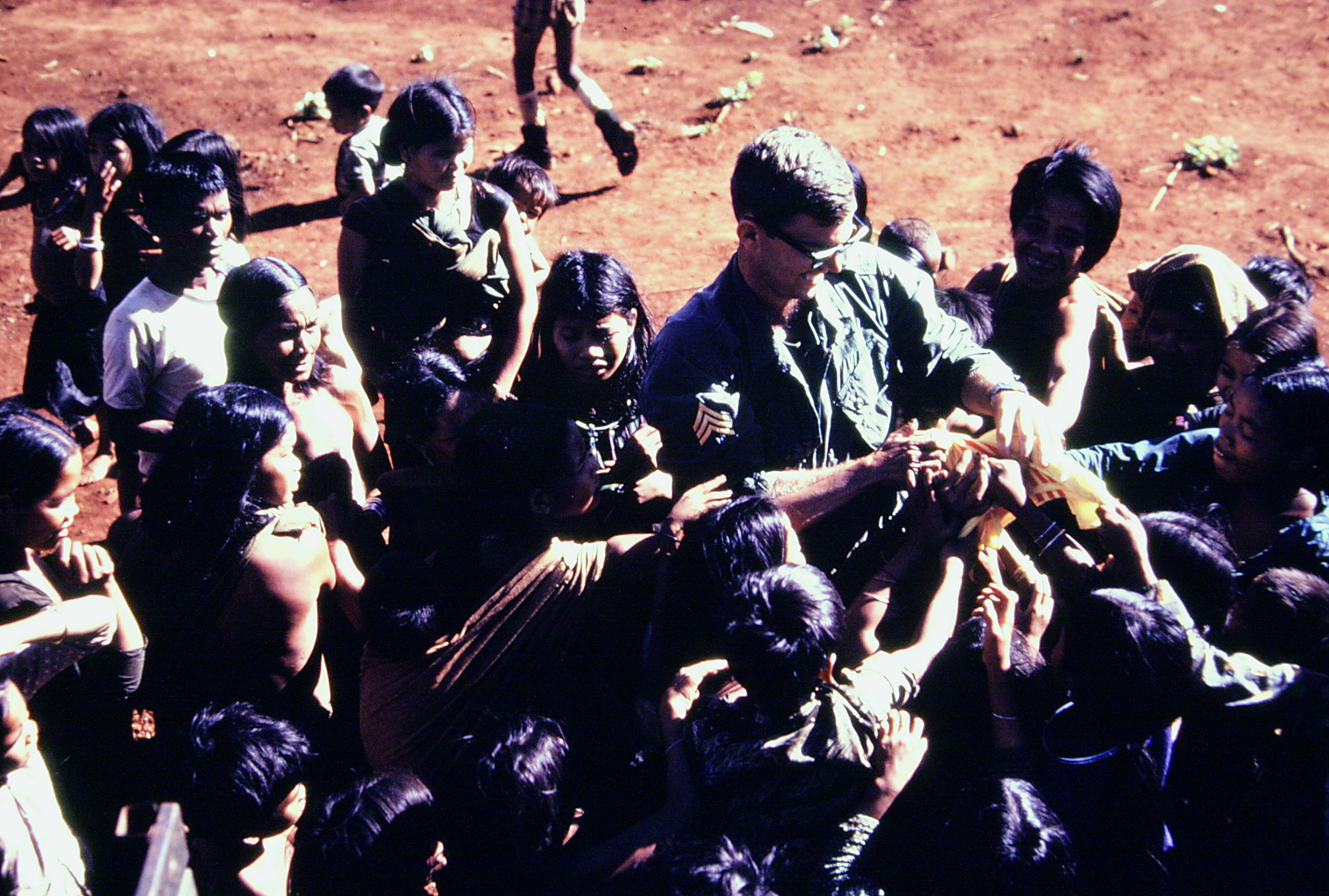 Young soldier surrounded by young Montagnard children in a military camp.