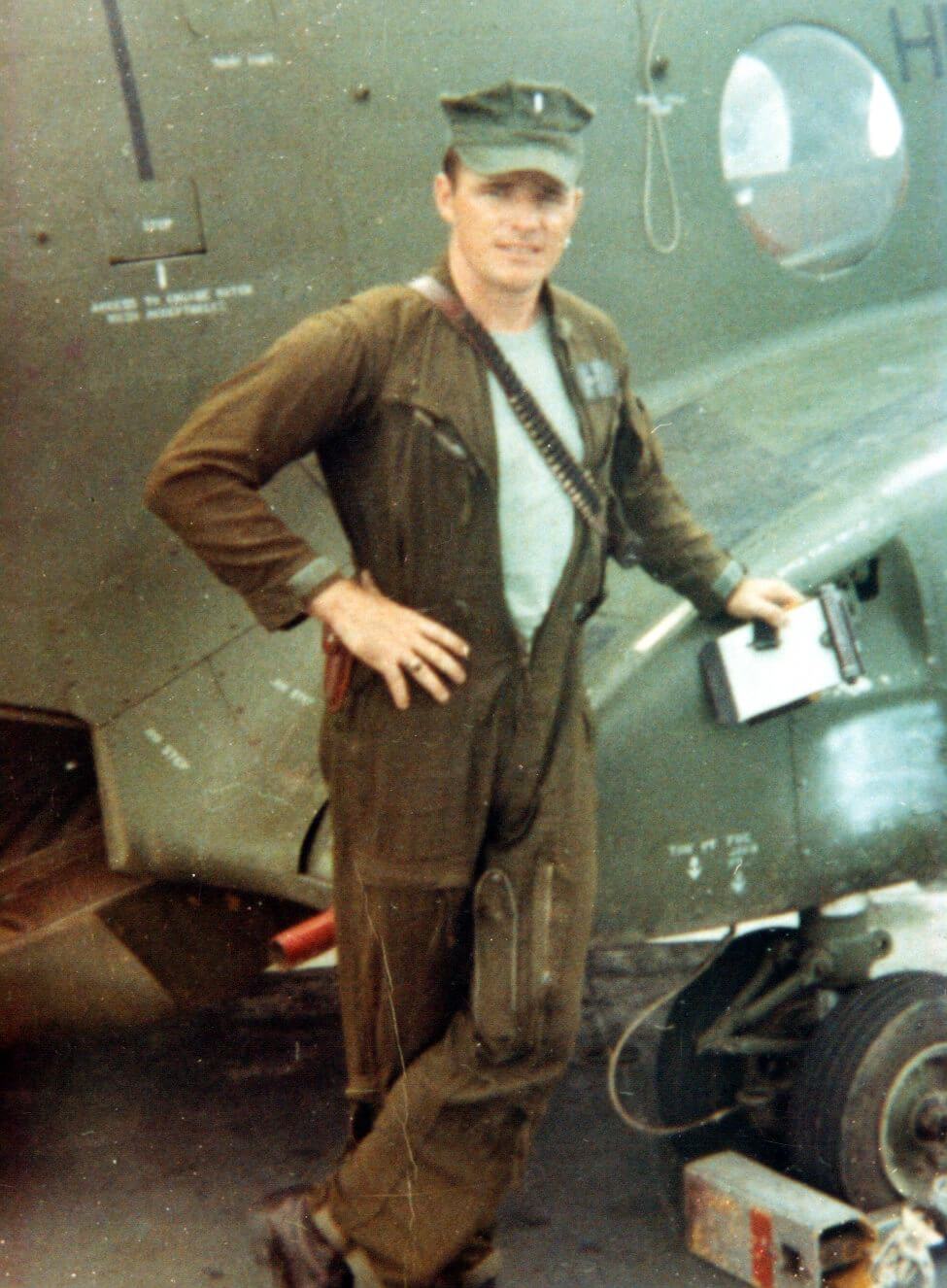 A young man standing in front of CH47, wearing a jumpsuit and a cap.