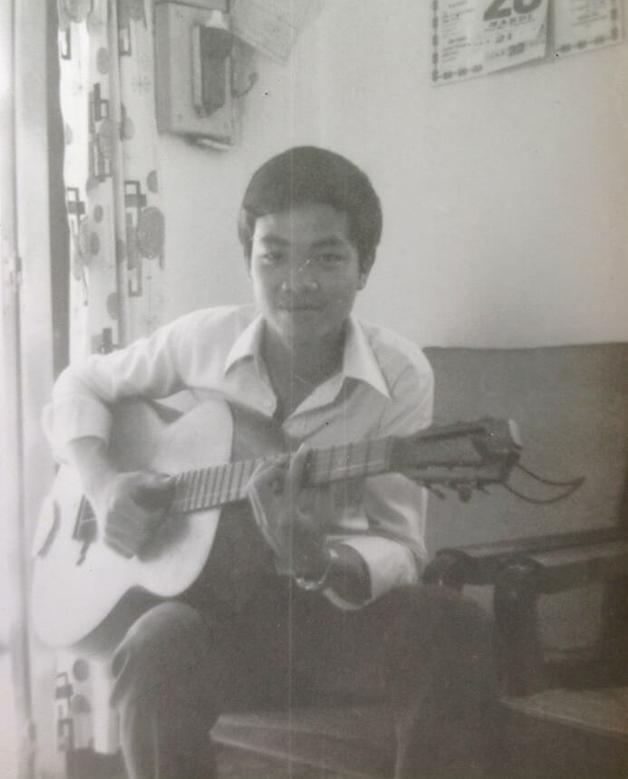 Black and white portrait of a young Vietnamese boy playing guitar.
