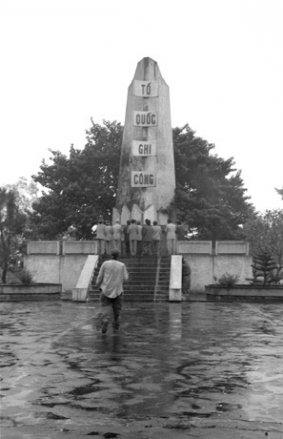 Black and white photo of some sort of memorial in a town square in Vietnam. Men in suits are gathered around it.