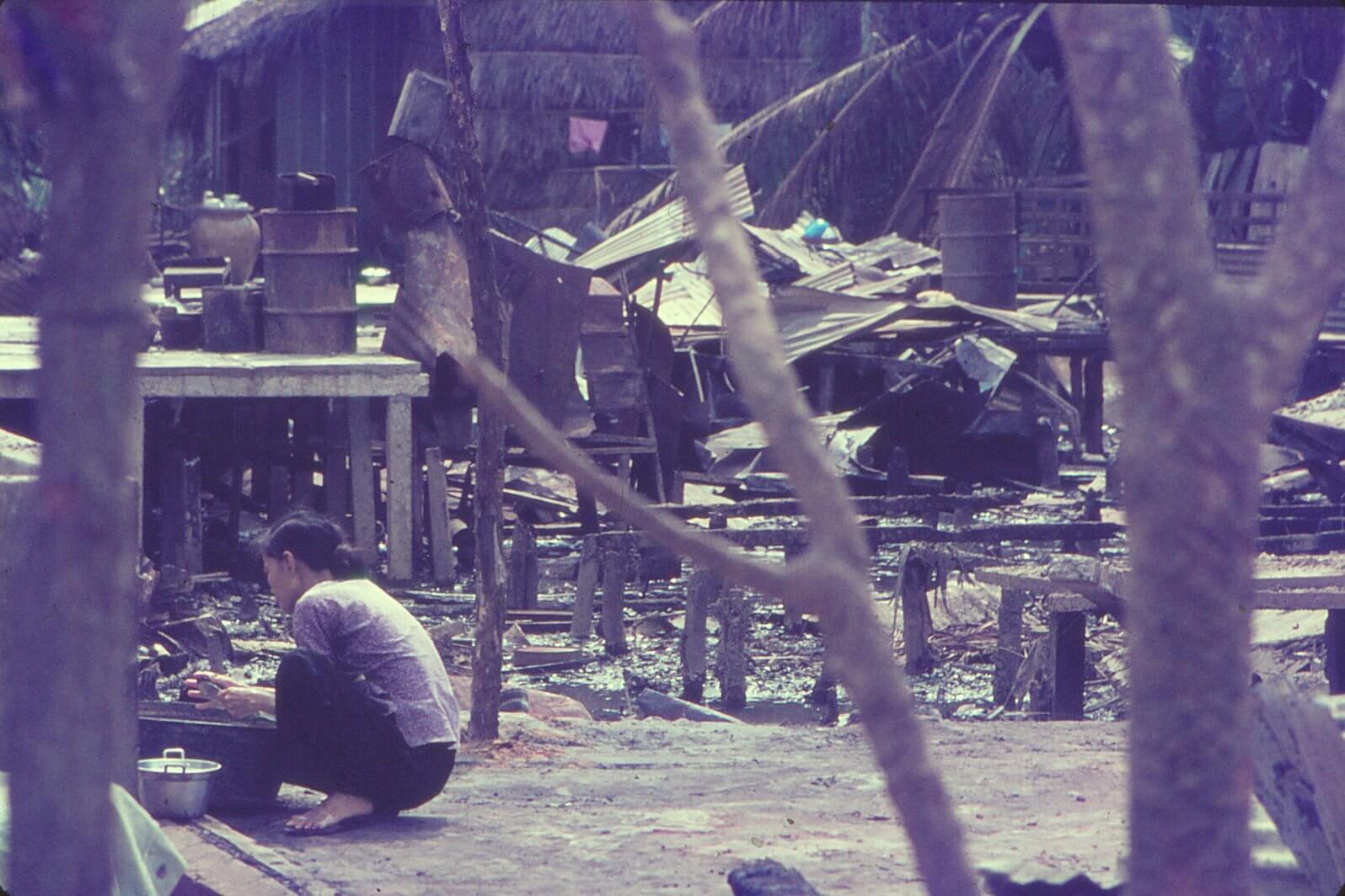 A Vietnamese woman squatting amid rubble.