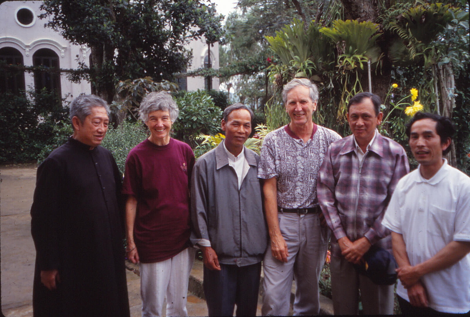 A white woman and man posing with 4 Asian men, one of the men in a black habit.