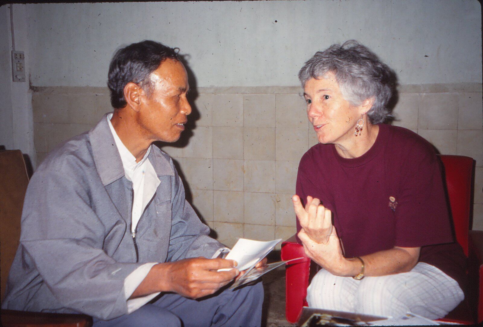 An older Vietnamese man and an older American woman talking and looking over what looks to be photos.