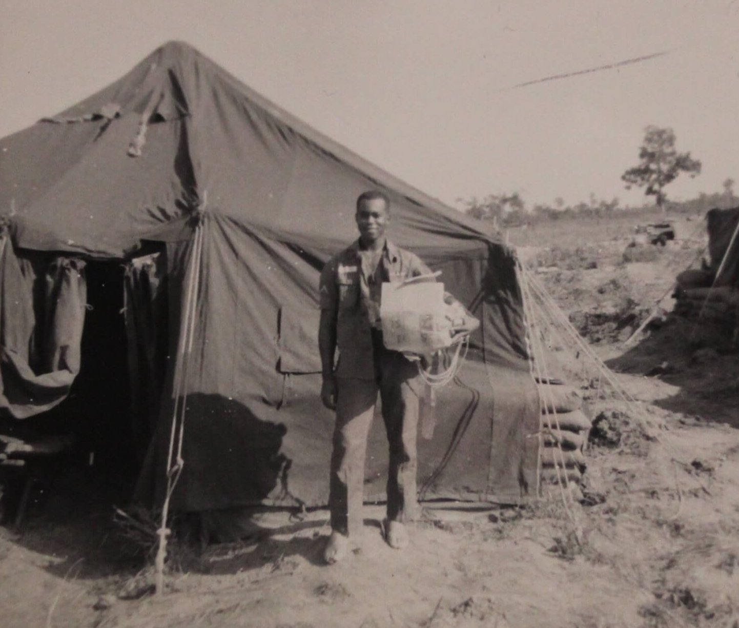 An African American soldier, standing outside a tent.