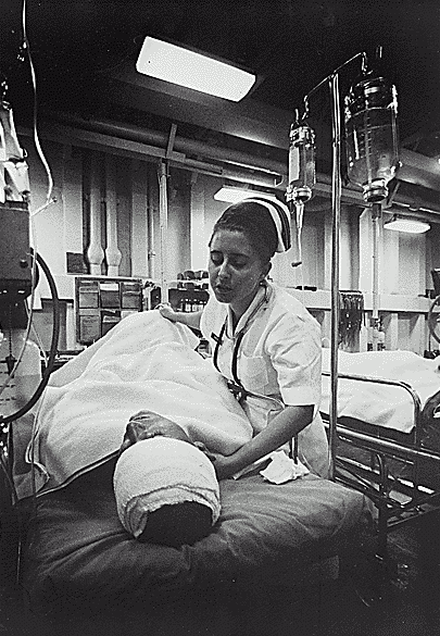 A nurse taking care of a soldier with a bandaged head. An IV drip is nearby.