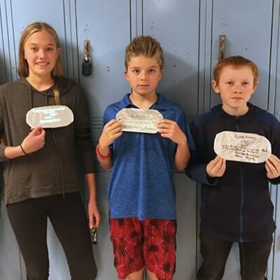 Contemporary photo of three school children holding up large "dog tags" they've made for class.