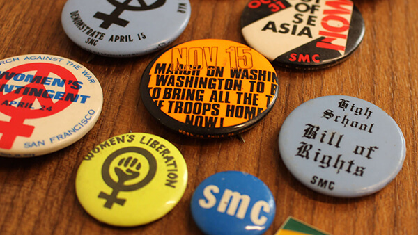 A color photo of a bunch of protest buttons laid out on a wooden table.