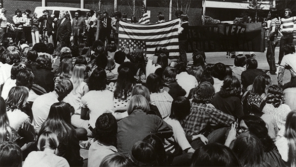 A crowd of student protesters; an upside down American flag in the background.