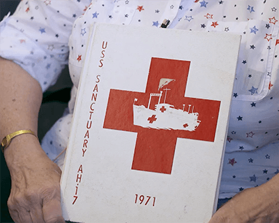 A USS Sanctuary 1971 yearbook being held in an older woman's lap.