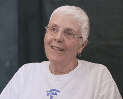 Contemporary image of an older woman with glasses and short white hair, smiling.