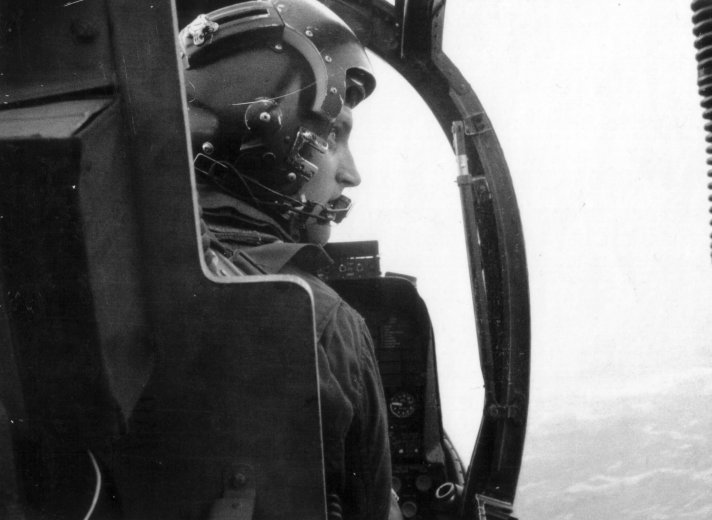Photo of a pilot wearing his helmet, up in his aircraft, taken from behind.