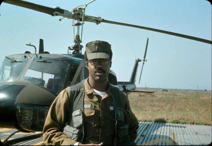 A young black pilot standing in front of a helicopter.