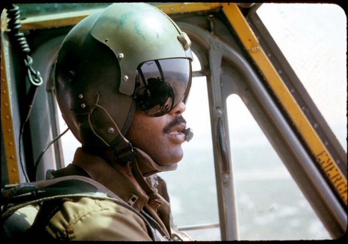 A young black pilot with his helmet on, sitting in the cockpit of his plane.