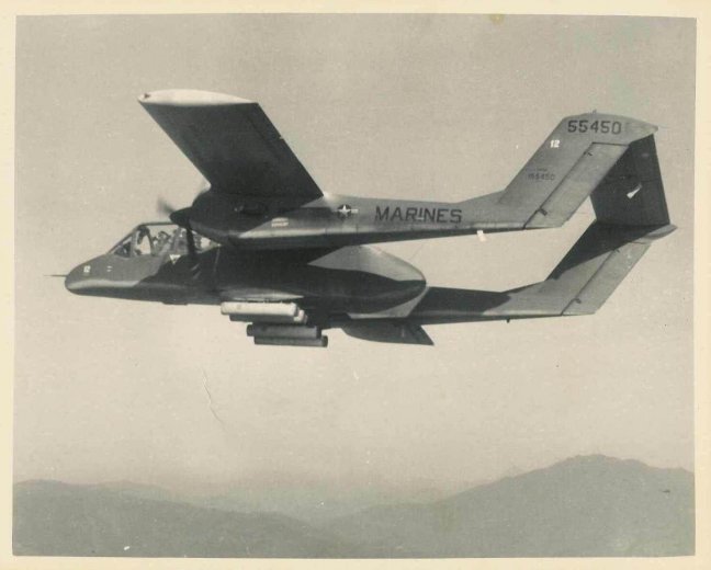 An aircraft that says "Marines 55450" in the air over mountainous land.