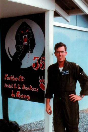 A young pilot in a jumpsuit, leaning against a sign that says "Panther Co Lt. Col L.L. Beckers Gang".
