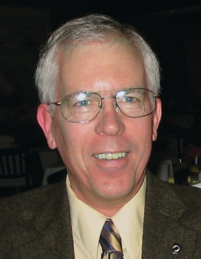 Contemporary portrait of an older gentleman in glasses and a suit, smiling at the camera.