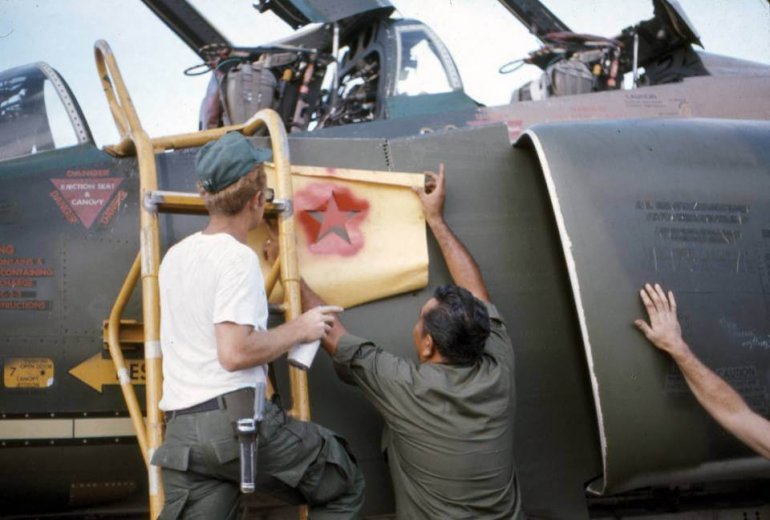 Soldiers stenciling the side of an aircraft with red stars.