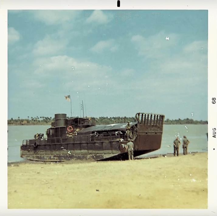 A small, broad boat that is pulled up to shore. Three soldiers stand nearby. Text on photo margins reads "Aug 68".