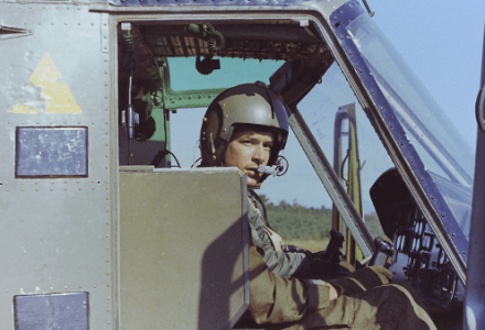 A young pilot in his helicopter, looking out towards the camera.