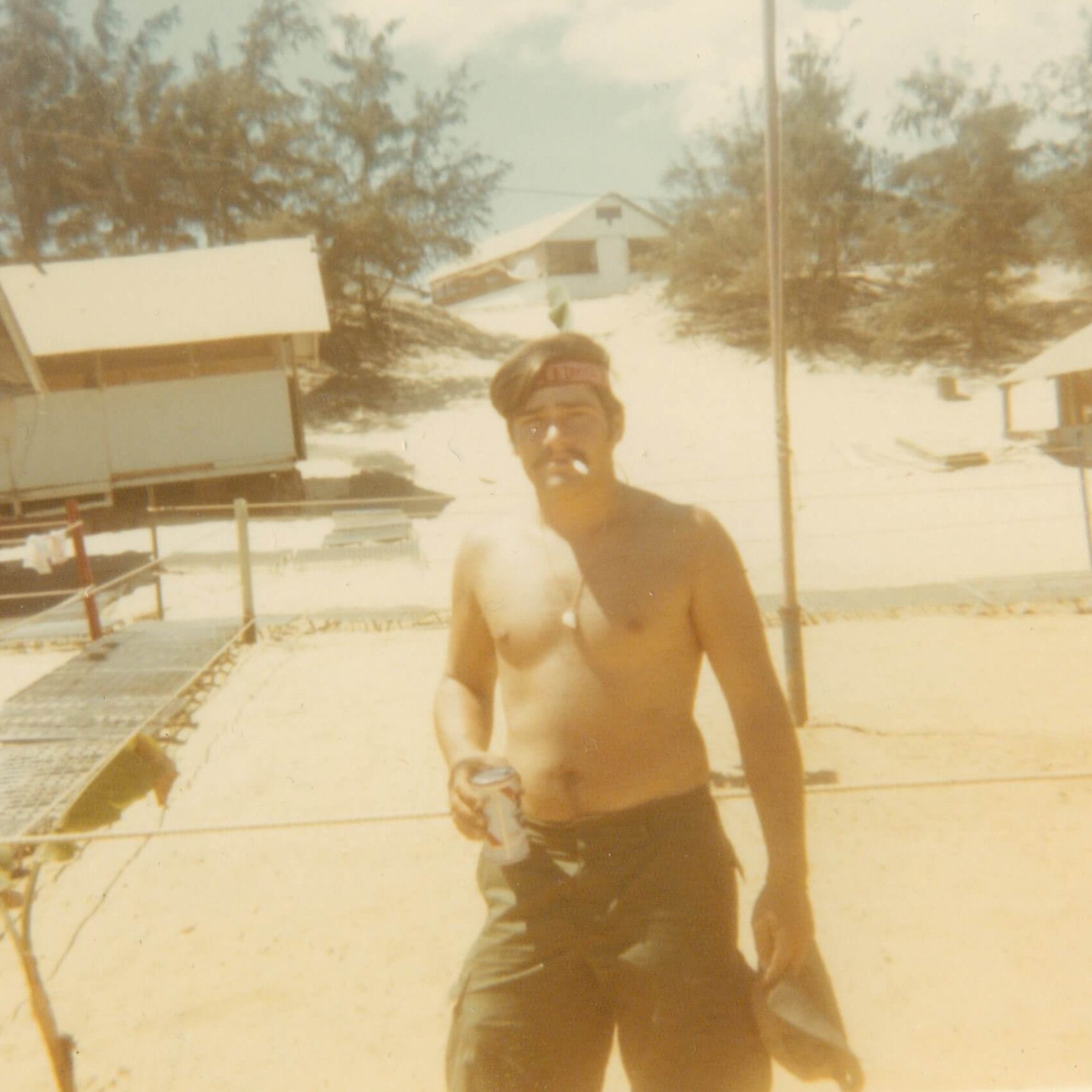 A shirtless soldier wearing a headband, smoking a cigarette, and holding a beer.