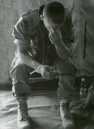 A soldier sitting inside a tent with his head in his hands.